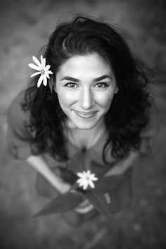 a black and white photo of a woman with a flower in her hair smiling at the camera