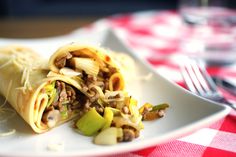 a burrito with meat, beans and vegetables on a plate next to a fork