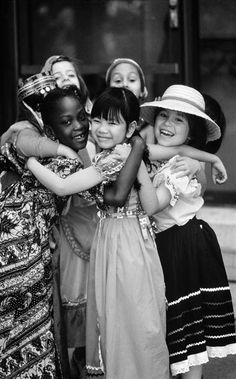 black and white photograph of four girls hugging each other with hats on their heads in front of a building