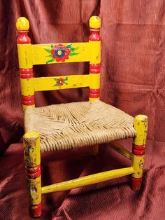 a yellow chair with red trim and flowers painted on the seat is against a brown background