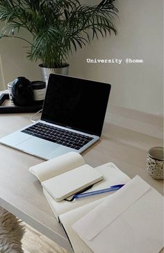 an open laptop computer sitting on top of a wooden desk next to a notebook and pen