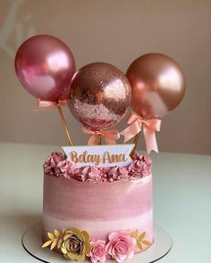 a pink and gold birthday cake with balloons on top