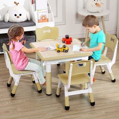 two children sitting at a table with toy cars on the table and one child writing