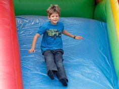 a young boy sliding down a slide in a bouncy house with blue tarp