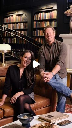 a man and woman sitting on a couch in front of a bookcase with books