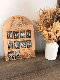 a wooden photo frame sitting on top of a table next to a vase filled with dried flowers