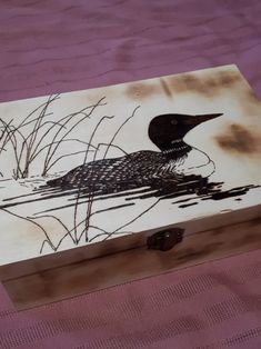 a wooden box with a painting of a bird on it's body and reeds in the water