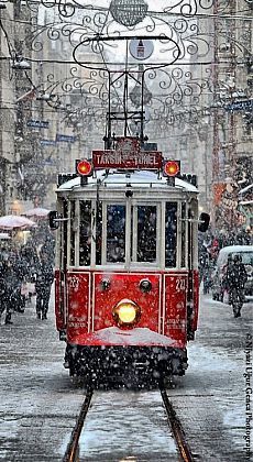 a red trolly car traveling down a snow covered street