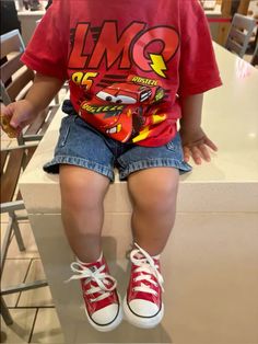 a little boy sitting on top of a counter next to a pair of red shoes