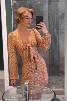 a woman taking a selfie in front of a bathroom mirror wearing a dress and holding a cell phone