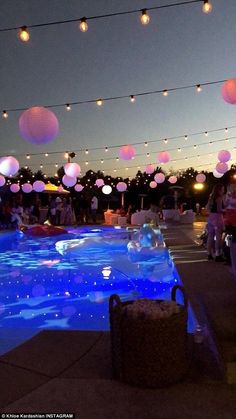 people are gathered around an inflatable swimming pool at night with paper lanterns strung above