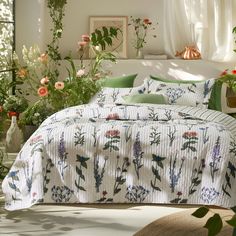 a bed covered in white and green floral comforter next to potted plants on the floor