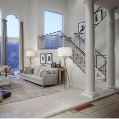 a living room filled with lots of furniture and tall windows next to a stair case