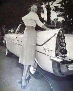 an old photo of a woman standing next to a car