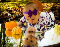 a baby girl with a purple bow on her head is reflected in a puddle next to pumpkins