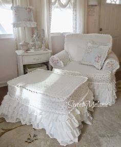 a white chair and footstool in a room with curtains on the windowsill