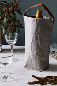 a wine bottle in a paper bag next to some glasses and utensils on a table