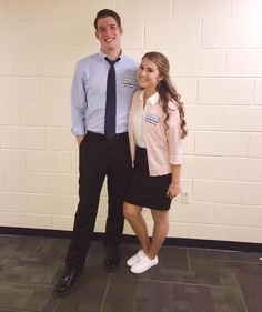 a man and woman standing next to each other in front of a white brick wall