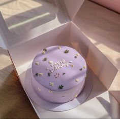 a purple cake in a white box with flowers on the top and happy birthday written on it