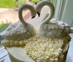 two white swans on top of a cake with frosting and icing petals in the shape of hearts