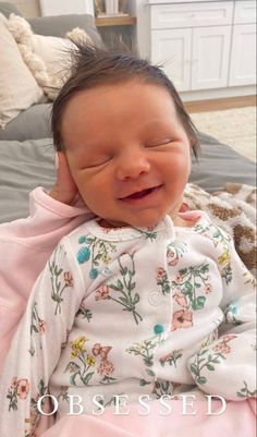 a baby laying on top of a bed wearing a pink blanket and smiling at the camera