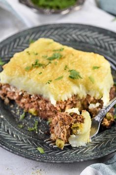 a piece of meat and cheese pie on a black plate with a fork in it