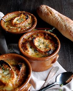 three small bowls filled with food next to a loaf of bread on top of a table