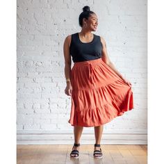 a woman standing in front of a white brick wall wearing an orange tiered skirt