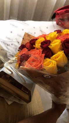 a person holding a bouquet of flowers on top of a bed next to a book