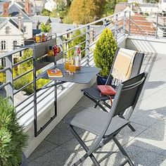 a balcony with two chairs and a table on top of it, overlooking the city