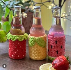 three crocheted soda bottles sitting on top of a table next to lemon slices