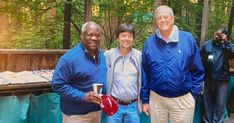 three men standing next to each other in front of trees