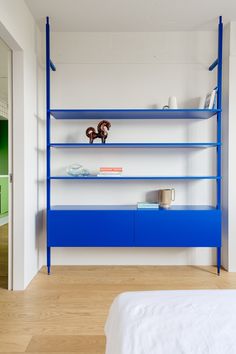 a blue shelf in the middle of a room with white walls and wood floors, along with a bed