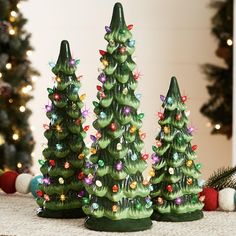 three green christmas trees with lights on them sitting in front of a decorated christmas tree