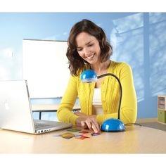 a woman sitting at a table with a laptop and lamp in front of her,