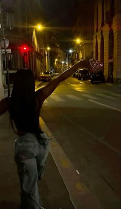 a woman holding her arms up in the air on a city street at night time