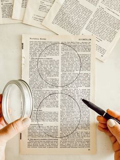 two hands holding a pen over an open book with circles drawn on it and some papers around them