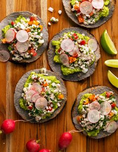 four tortillas topped with veggies and radishes on a wooden table