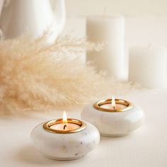 two white marble candles sitting next to each other on a table with some feathers in the background