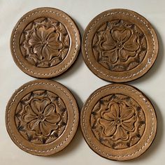 four brown leather coasters with floral designs on them