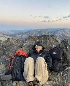 a man sitting on top of a mountain next to backpacks