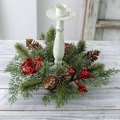 a white candle holder with pine cones and berries