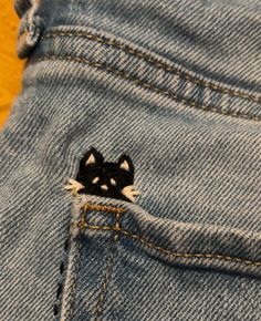 A black cat with white eyes and whiskers embroidered into jeans Embroidery Jean Pocket Ideas, Pretty Embroidery Designs, Cute Stitches On Clothes, Jeans Back Pocket Embroidery, Black Jeans Embroidery Ideas, Embroidered Jeans Diy Simple, Cute Small Embroidery, Custom Diy Ideas, Punk Embroidery Ideas