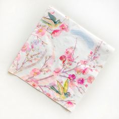 a napkin with flowers and birds on it sitting on a white tablecloth that is folded in half