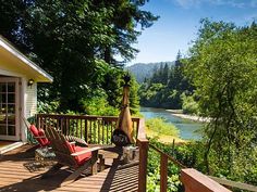 there is a deck with two chairs on it next to the water and trees in the background