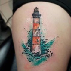 a woman's thigh with a watercolor painting style lighthouse tattoo on her leg