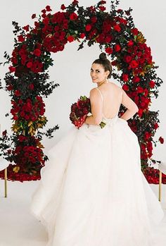 a woman in a wedding dress standing next to a floral arch with roses on it