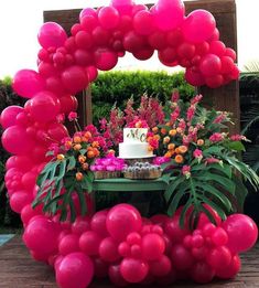 a table topped with pink balloons and a cake surrounded by greenery on top of it