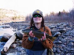 a woman holding a fish in her hands while standing next to a river and rocks