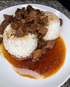 a white plate topped with meat and rice covered in gravy on top of a table